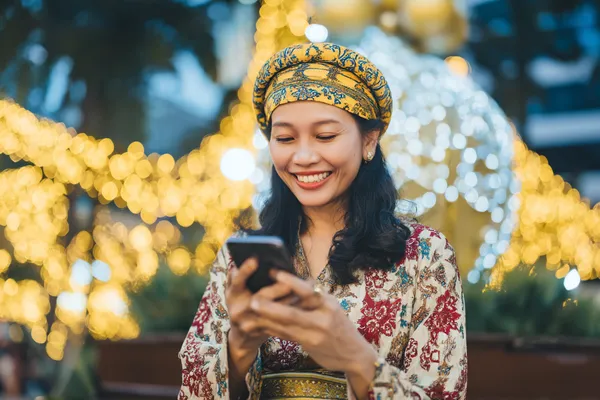 A cheerful woman in traditional clothing using her smartphone during a festive moment, showing how easily the CD444 app fits into everyday life.