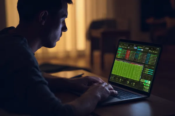 A man focused on his laptop with live stats in the background, highlighting the dedicated sports and gaming features of the CD444 mobile app.